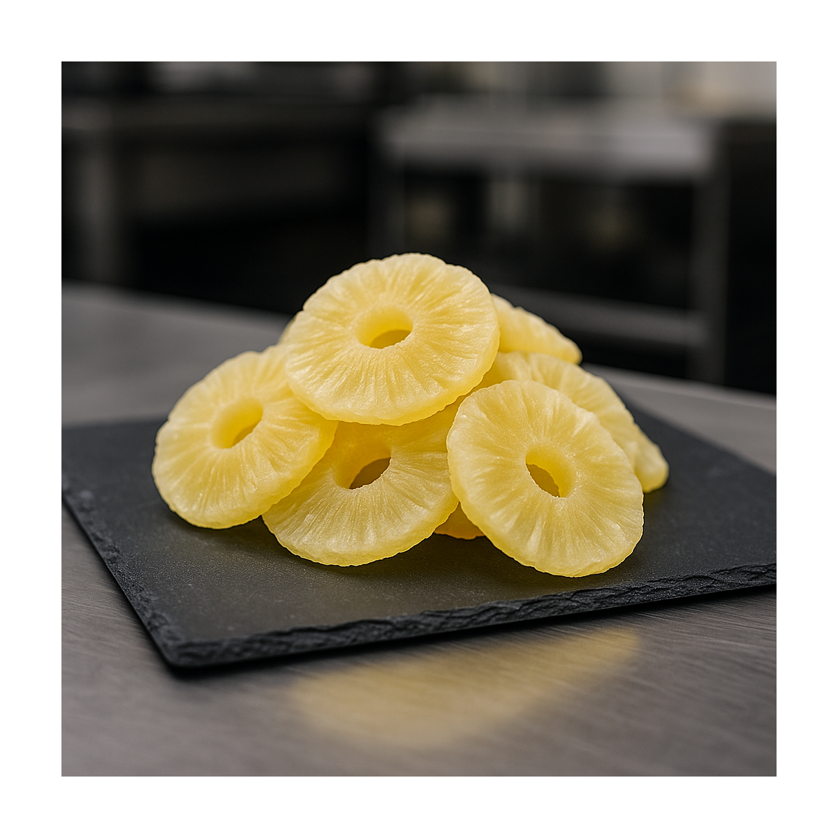 Natural dried pineapple slices displayed on slate in a stainless-steel pro kitchen